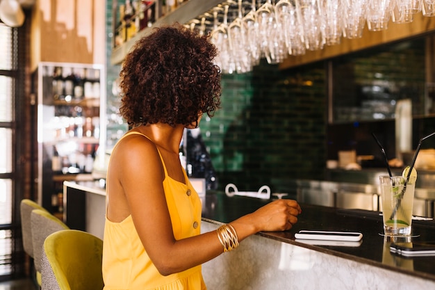 Photo gratuite femme aux cheveux courts et bouclés, assise près du comptoir avec smartphone