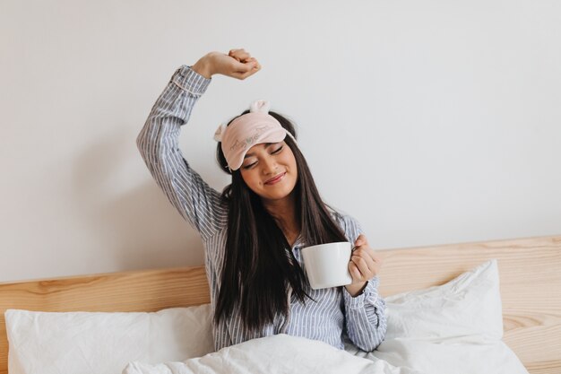 Femme aux cheveux longs en pyjama bleu s'étire doucement après avoir dormi