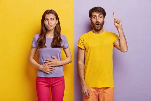 Femme aux cheveux noirs affamée touche l'estomac, veut manger quelque chose de savoureux, porte un t-shirt violet et un pantalon rose