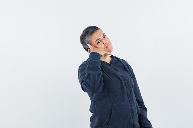 Femme aux cheveux noirs montrant le geste d'appel téléphonique en veste et à la satisfaction