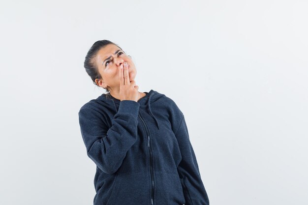 Femme aux cheveux noirs tenant la main sur la bouche en veste et à la réflexion