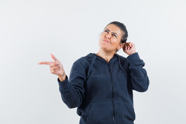 Femme aux cheveux noirs tenant la main sur la tête tout en pointant de côté dans la veste et à la confusion