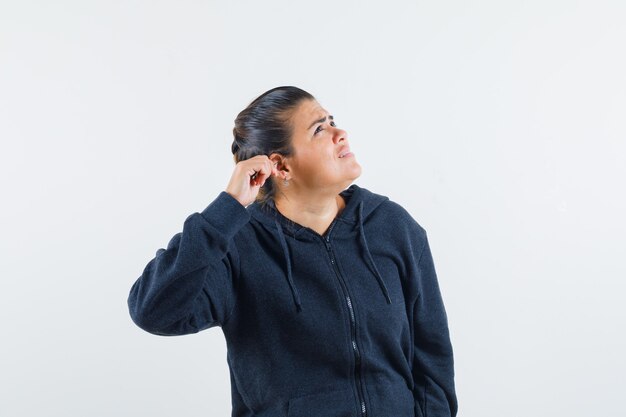 Femme aux cheveux noirs en veste tenant la main sur l'oreille et à la recherche concentrée