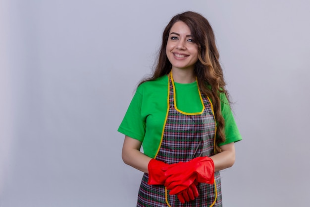 Femme aux longs cheveux ondulés portant un tablier et des gants en caoutchouc souriant avec un visage heureux debout