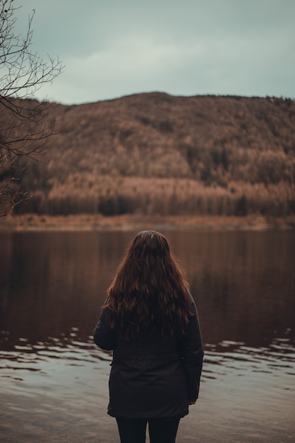 femme aux longs cheveux roux debout près d'un lac dans une forêt