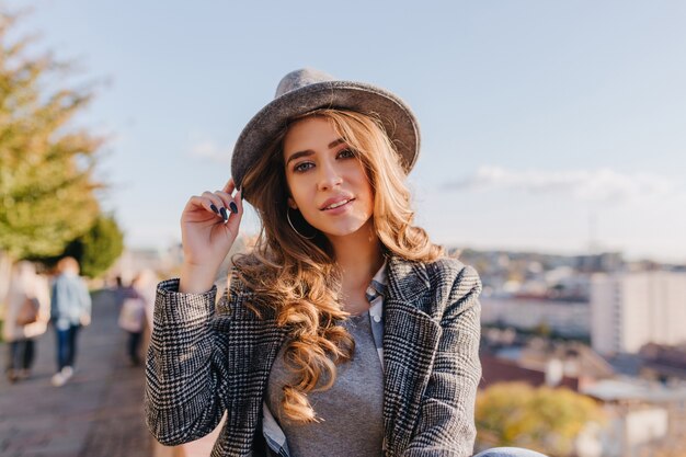 Femme aux yeux bleus intéressée en chapeau à la mode posant pendant la promenade du matin