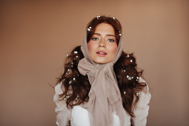 Femme aux yeux verts en chemisier blanc et avec de petites fleurs dans les cheveux posant. femme en foulard regarde la caméra.