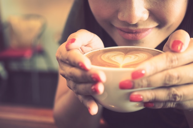 Femme ayant une tasse de café avec un coeur dessiné dans la mousse