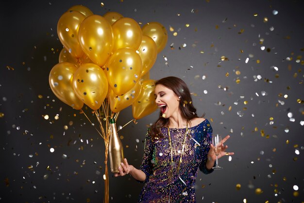Femme avec des ballons et du champagne parmi les confettis