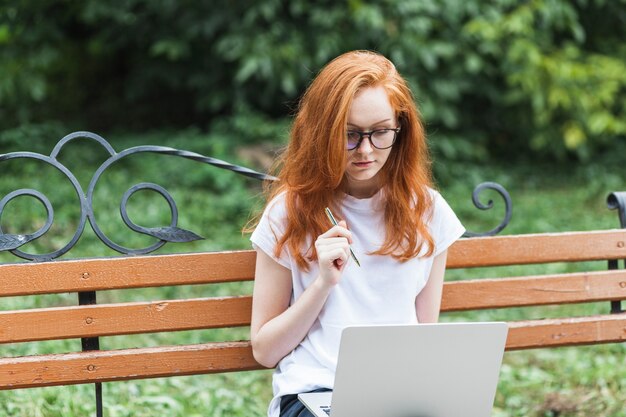 Femme sur banc avec ordinateur portable et stylo