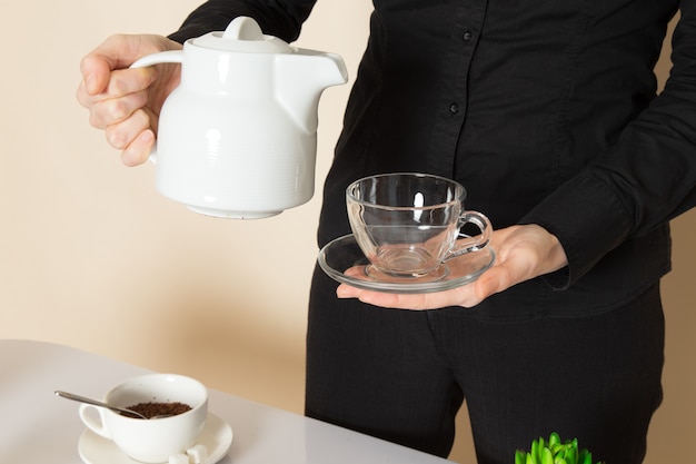 Femme barista en pantalon chemise noire avec des ingrédients de l'équipement de thé séché brun café sur le mur blanc