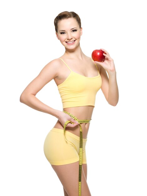 Femme avec un beau corps sportif mince mesurant la wistline et tenant une pomme rouge fraîche. Portrait isolé sur blanc