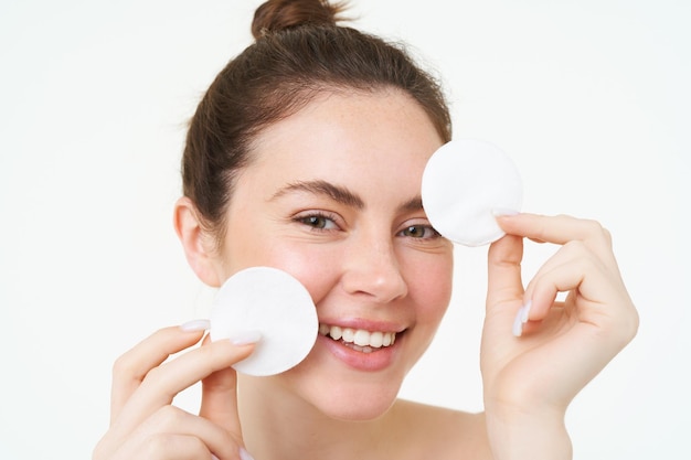 Photo gratuite une femme de beauté avec un visage brillant et clair montrant des tampons cosmétiques en coton pour le démaquillage qui la nettoient