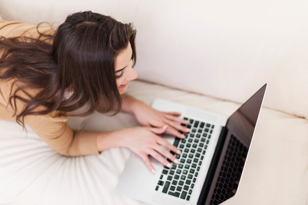 Femme bénéficiant de temps libre avec ordinateur portable sur canapé