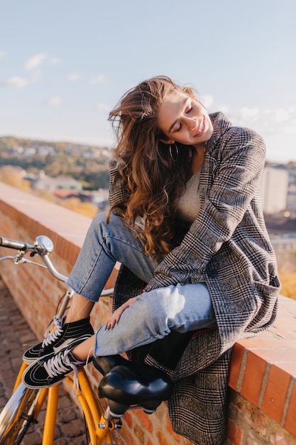 Femme blanche détendue en jeans décontracté assis sur le mur avec les yeux fermés