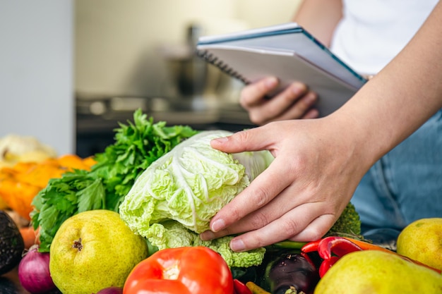 Femme avec bloc-notes et légumes sur la table de la cuisine préparant une recette