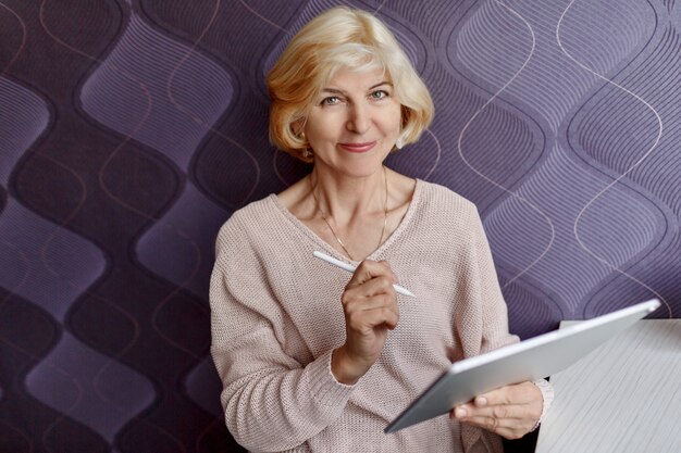 Femme blonde d'âge moyen souriante avec tablette