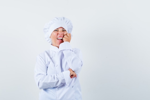 Femme blonde appuyée sur la joue sur la paume, souriant en uniforme de cuisinier blanc et à la jolie.