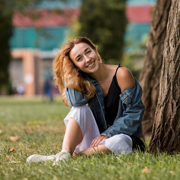 Femme blonde assise à côté d'un arbre