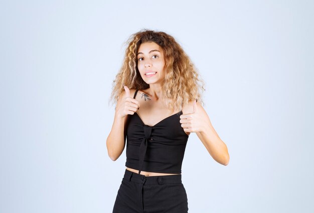 Femme blonde aux cheveux bouclés montrant un bon signe de la main.