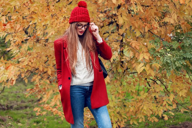 Femme blonde aux cheveux longs marchant dans le parc automne ensoleillé en tenue décontractée à la mode.