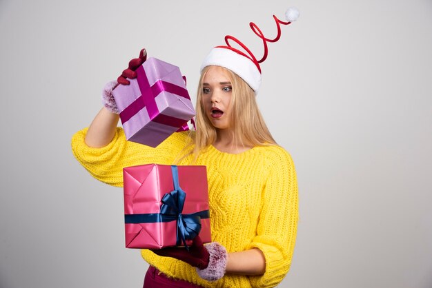 Femme blonde en bonnet de Noel regardant les cadeaux de Noël de manière surprenante.