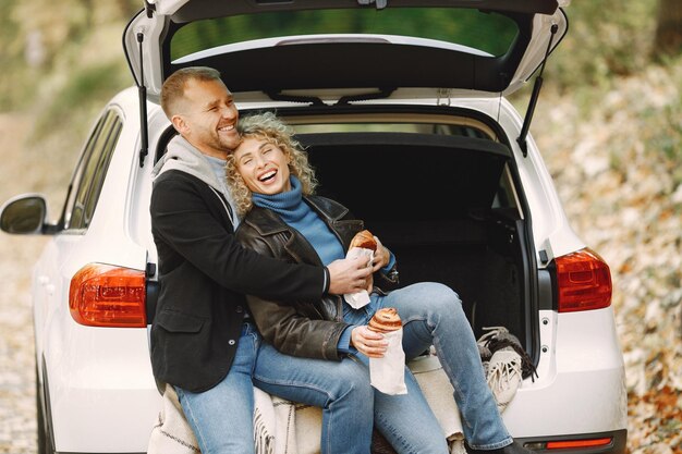 Femme blonde bouclée et homme assis dans un coffre en voiture dans la forêt d'automne et s'étreindre