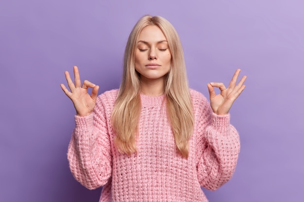 Une femme blonde calme soulagée cherche la paix à l'intérieur fait que le geste mudra atteint le nirvana et respire profondément les yeux fermés