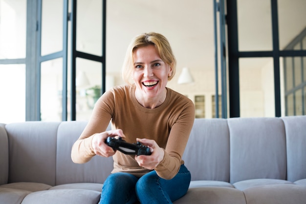 Femme blonde sur un canapé jouant à la console de jeu