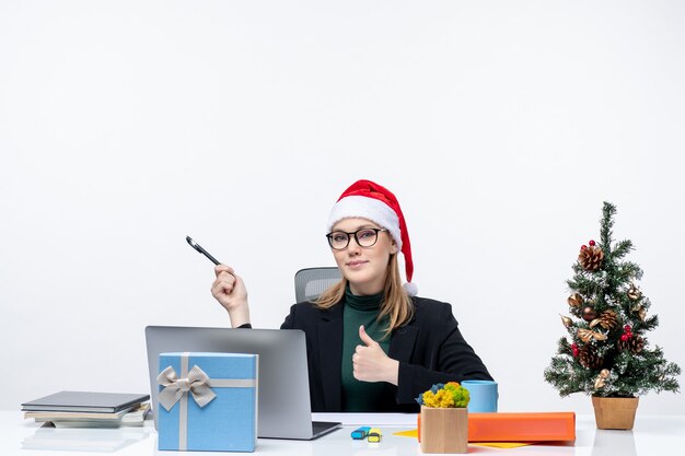 Femme blonde avec un chapeau de père Noël assis à une table avec un arbre de Noël et un cadeau