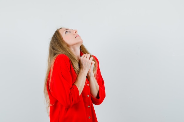 Femme blonde en chemise rouge, serrant les mains en geste de prière et à l'espoir,