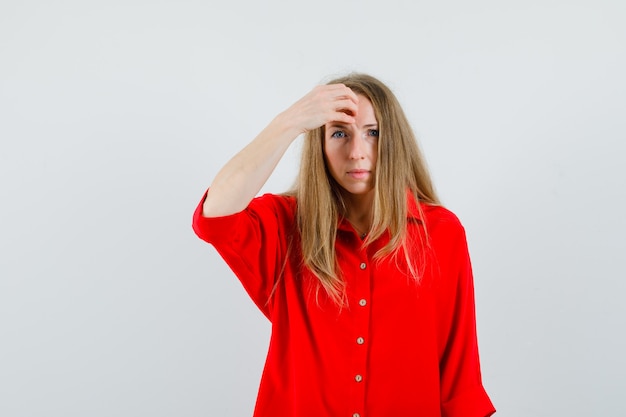 Femme blonde en chemise rouge tenant la main sur le front et à la confusion,