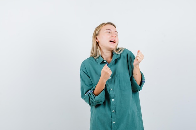 Femme blonde en chemise verte montrant le geste du gagnant et à la béatitude