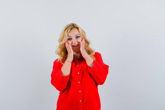 Femme blonde en chemisier rouge, main dans la main sur la joue et l'air heureux