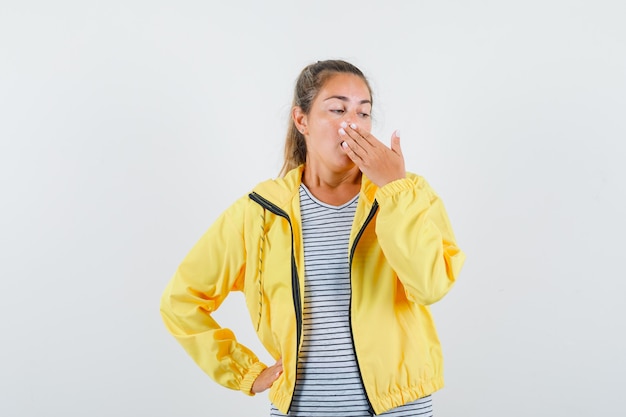 Photo gratuite femme blonde couvrant la bouche avec les mains en blouson aviateur jaune et chemise rayée et à la surprise