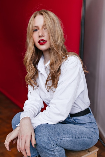 Femme blonde curieuse en jeans regardant la caméra Prise de vue en studio d'un modèle féminin glamour en chemise blanche