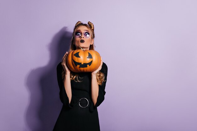 Femme blonde dans des verres tenant la citrouille d'halloween. photo d'une jeune sorcière inquiète.