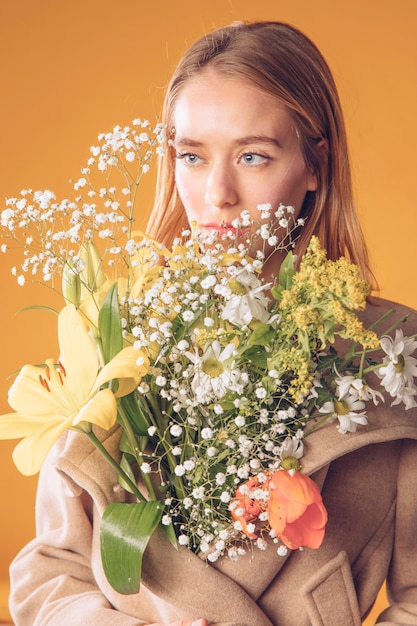 Femme blonde debout avec bouquet de fleurs en manteau