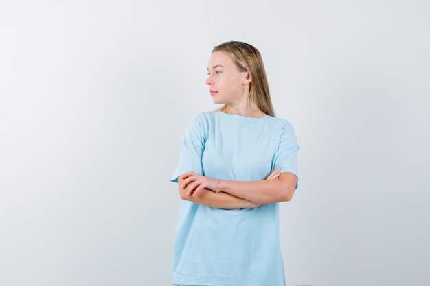 Femme blonde debout les bras croisés, regardant loin en t-shirt bleu et l'air mignon