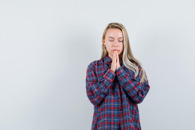 Femme blonde debout dans la prière pose en chemise à carreaux et à la vue de face focalisée