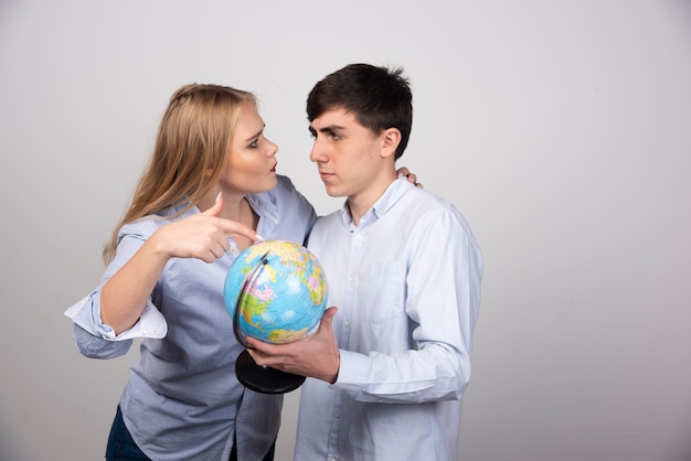 Femme blonde debout et pointant vers le globe terrestre près de mec brune