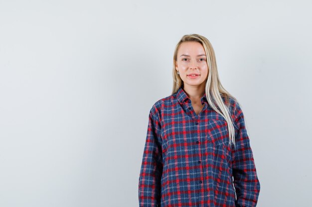 Femme blonde debout tout droit et posant à la caméra en chemise à carreaux et à la vue de face attrayante.