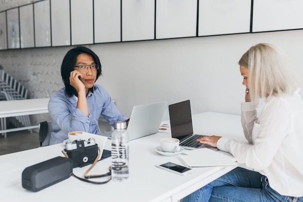 Photo gratuite femme blonde développeur web tapant sur le clavier, assis devant un étudiant asiatique dans des verres