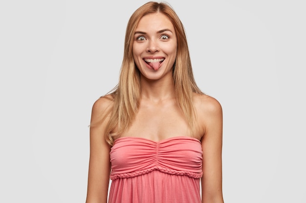 Femme blonde drôle fait la grimace à la caméra, tire la langue, montre une grimace, a une expression ludique