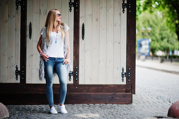 Une femme blonde élégante porte un jean et une fille sans manches avec une chemise blanche contre la rue