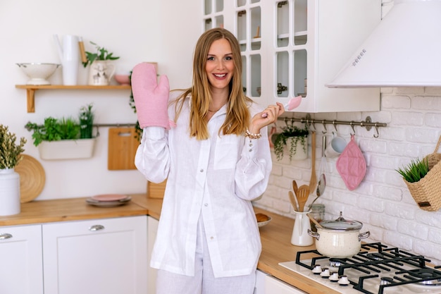 Femme blonde élégante posant dans sa jolie cuisine portant un pyjama en lin blanc.