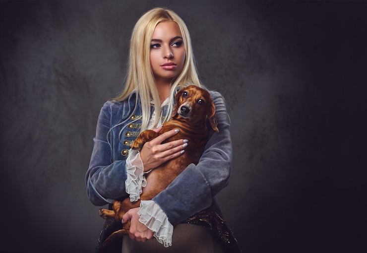 Photo gratuit une femme blonde élégante vêtue d'une veste à l'ancienne tient un chien blaireau rouge.