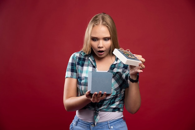 Une femme blonde est surprise en ouvrant un coffret cadeau.