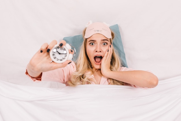 Femme blonde étonnée posant avec horloge