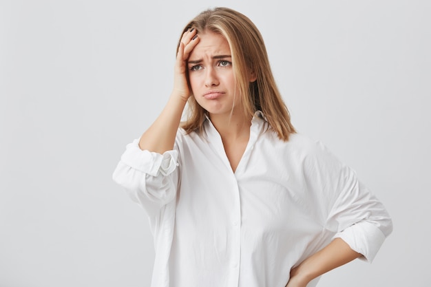 Femme Blonde Frustrée Portant Des Vêtements Décontractés, Tenant La Main Sur Le Front, Déprimé, Regrettant Quelque Chose, Ayant Des Maux De Tête.